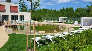 A pool area with lounge chairs, a small pond, and a building with red awnings. - Hotel Rittmeister (Rostock)