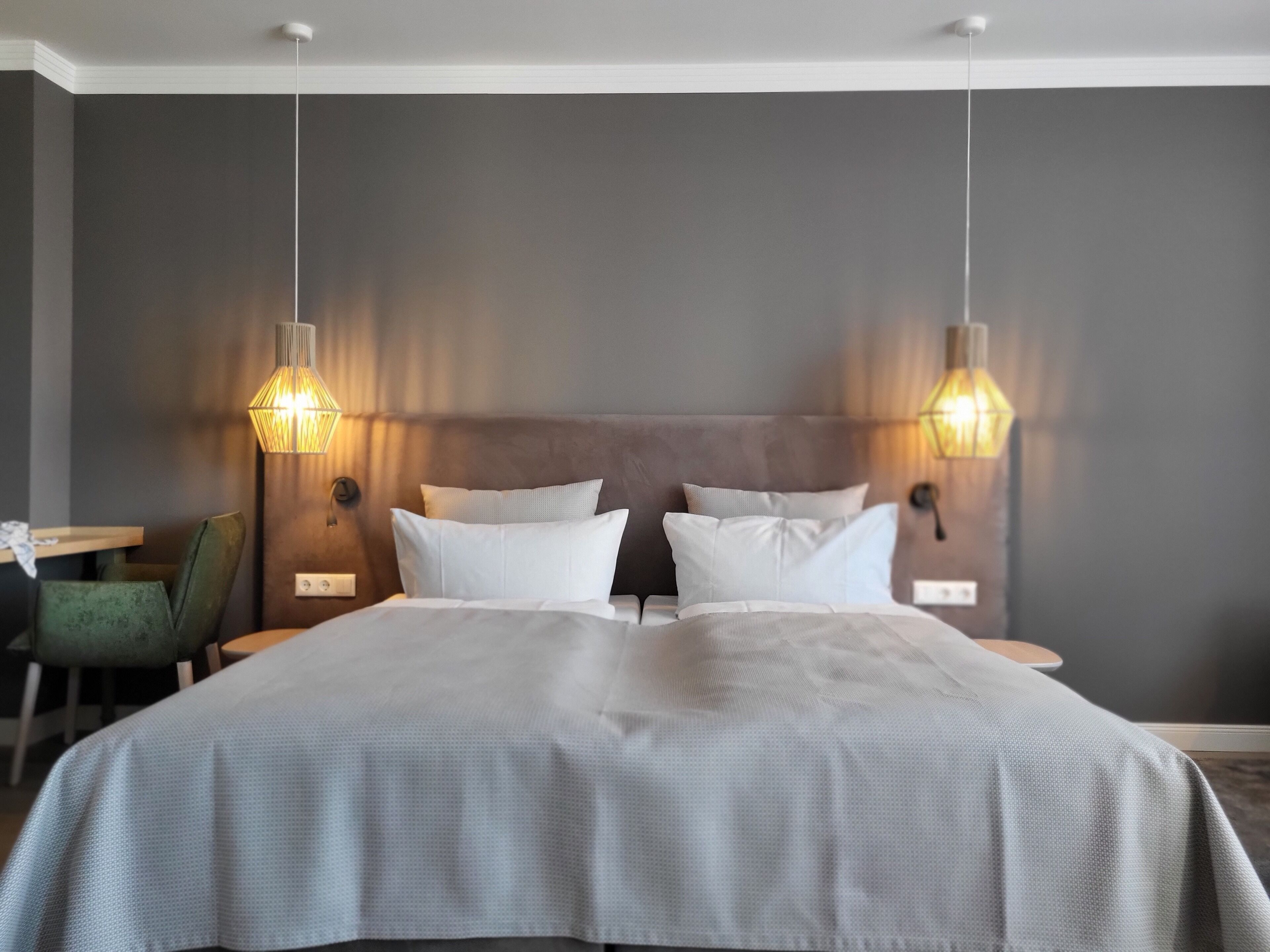 A modern hotel room with a large bed, two bedside lamps, a green chair, and a small table.