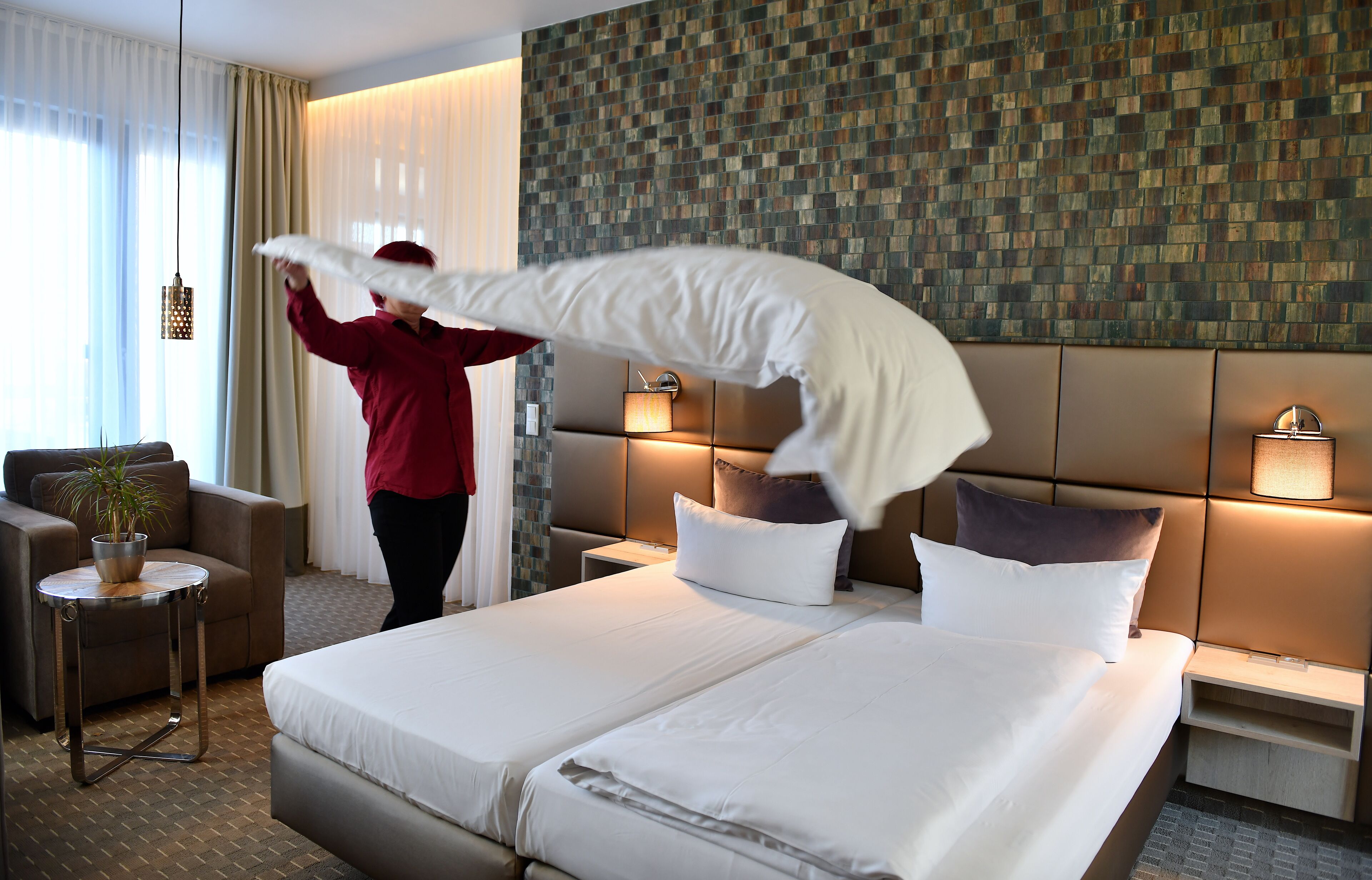 Une chambre d’hôtel avec un grand lit, un canapé, une petite table avec une plante et un mur orné d’un motif décoratif.