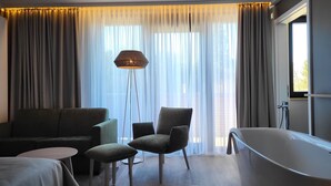 A modern bathroom with a freestanding bathtub, a sofa, two armchairs, and a floor lamp. - Hotel Rittmeister (Rostock)