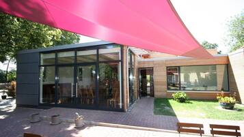 A modern building with large glass windows, a brick patio, and outdoor seating.