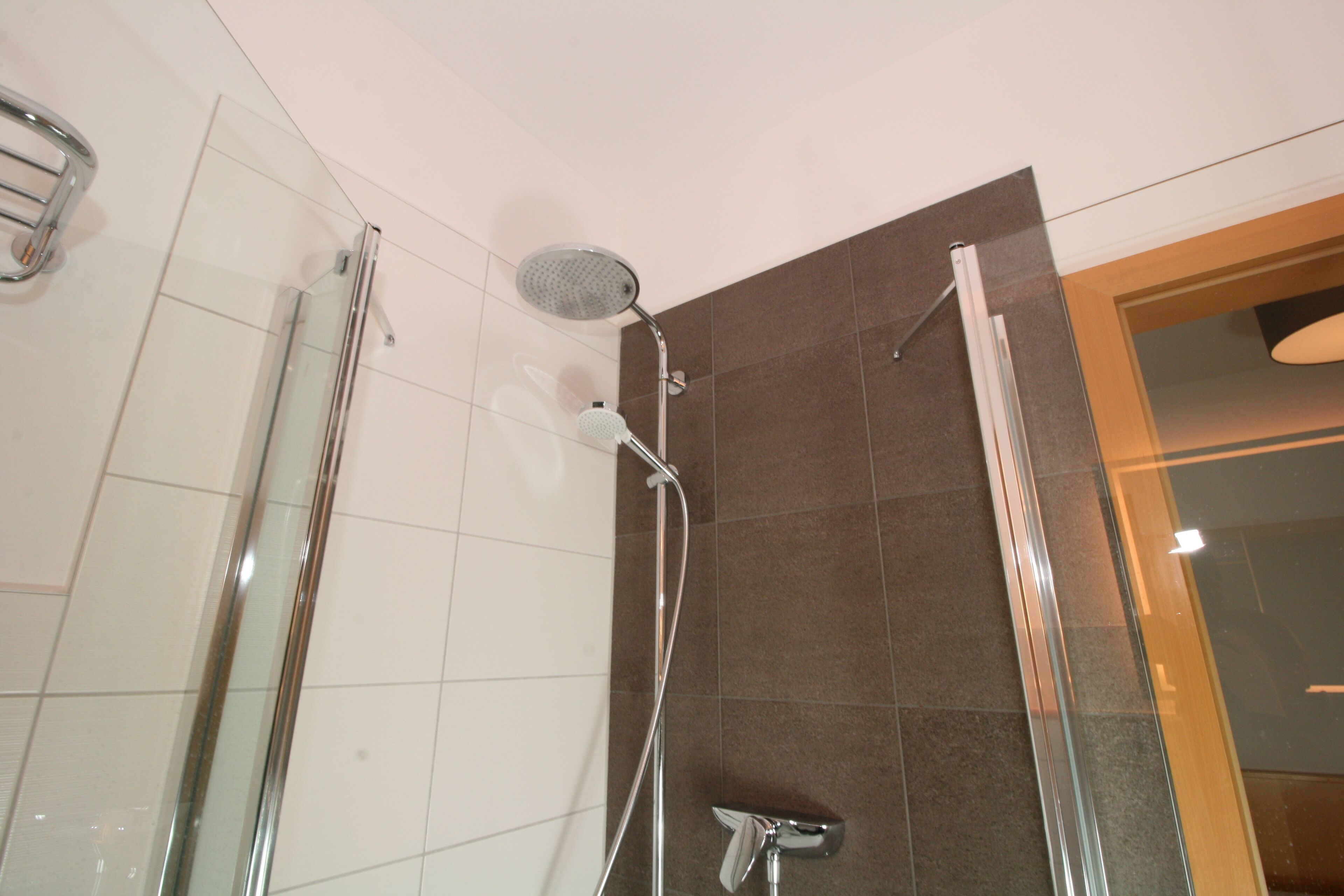 Ein modernes Badezimmer mit einer Glaskabine, einer Handbrause und einem wandmontierten Wasserhahn.