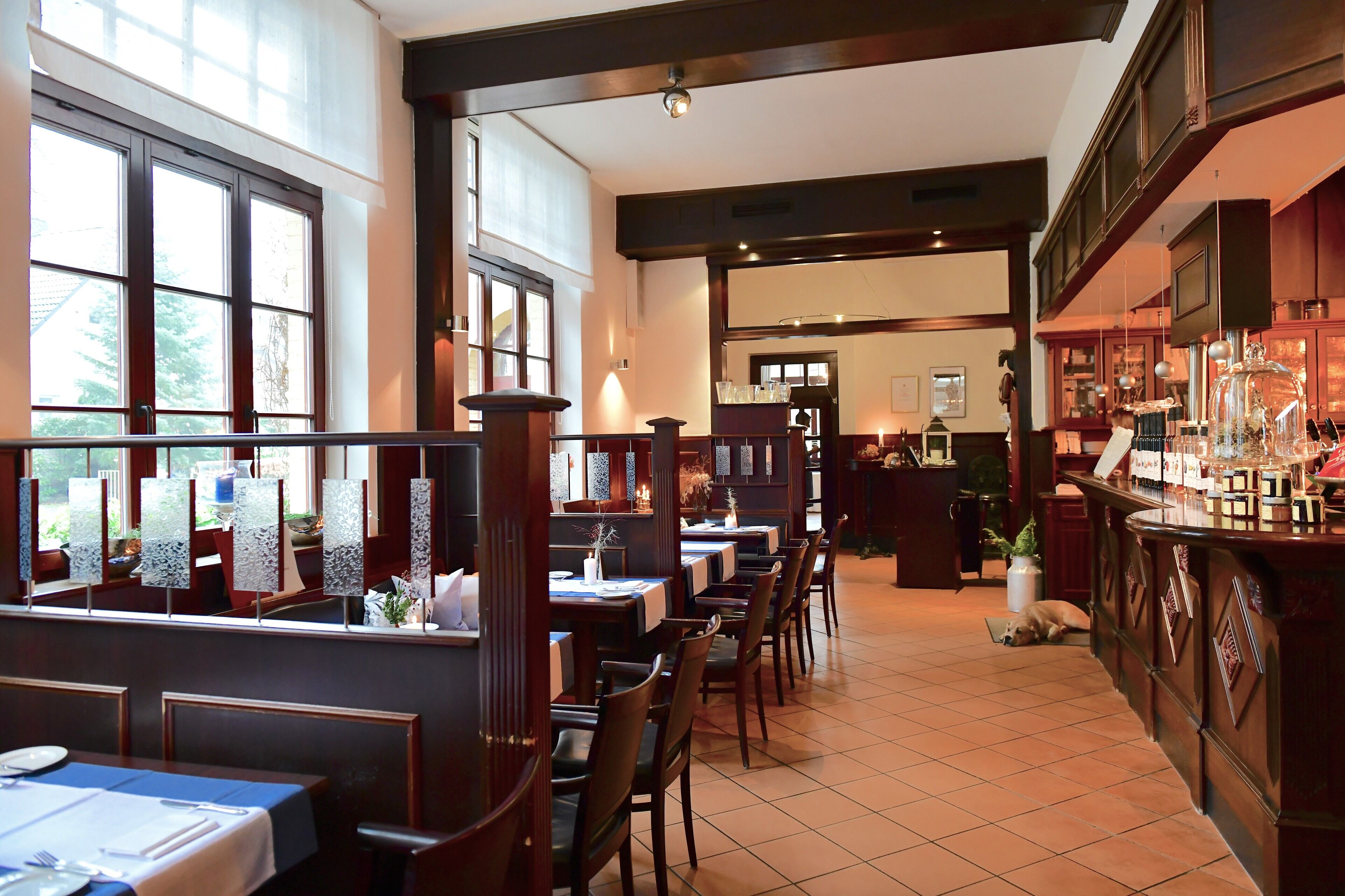 Un restaurant amb diverses taules i caires per seure, una zona de bar i vistes cap a l'exterior a través de grans finestres.