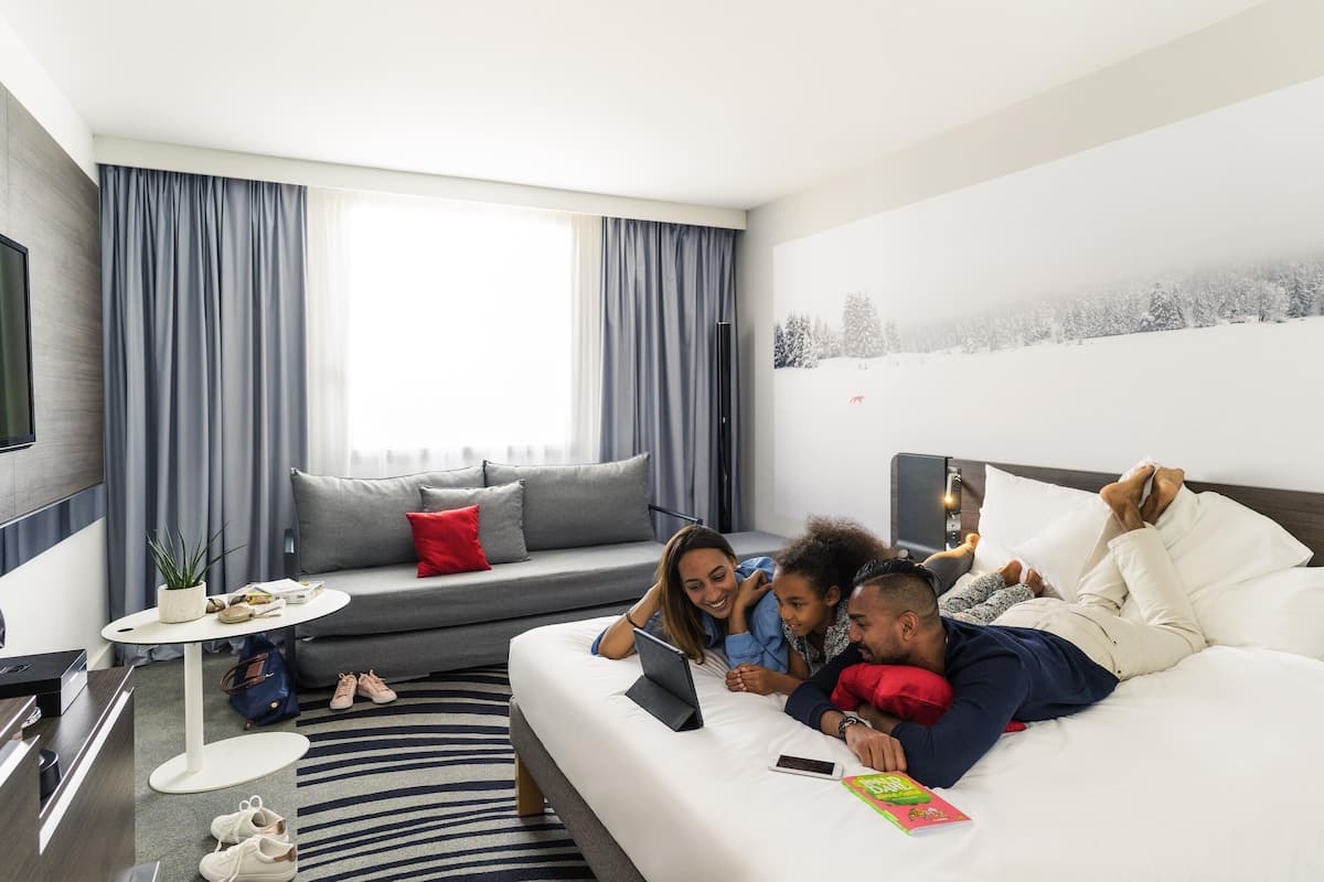 Una habitación de hotel moderna con sofá, televisión de pantalla plana, una pequeña mesa y una cama.