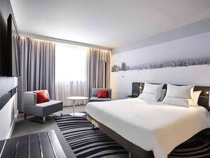A modern hotel room with a large bed, a sofa, a small table, and a TV.