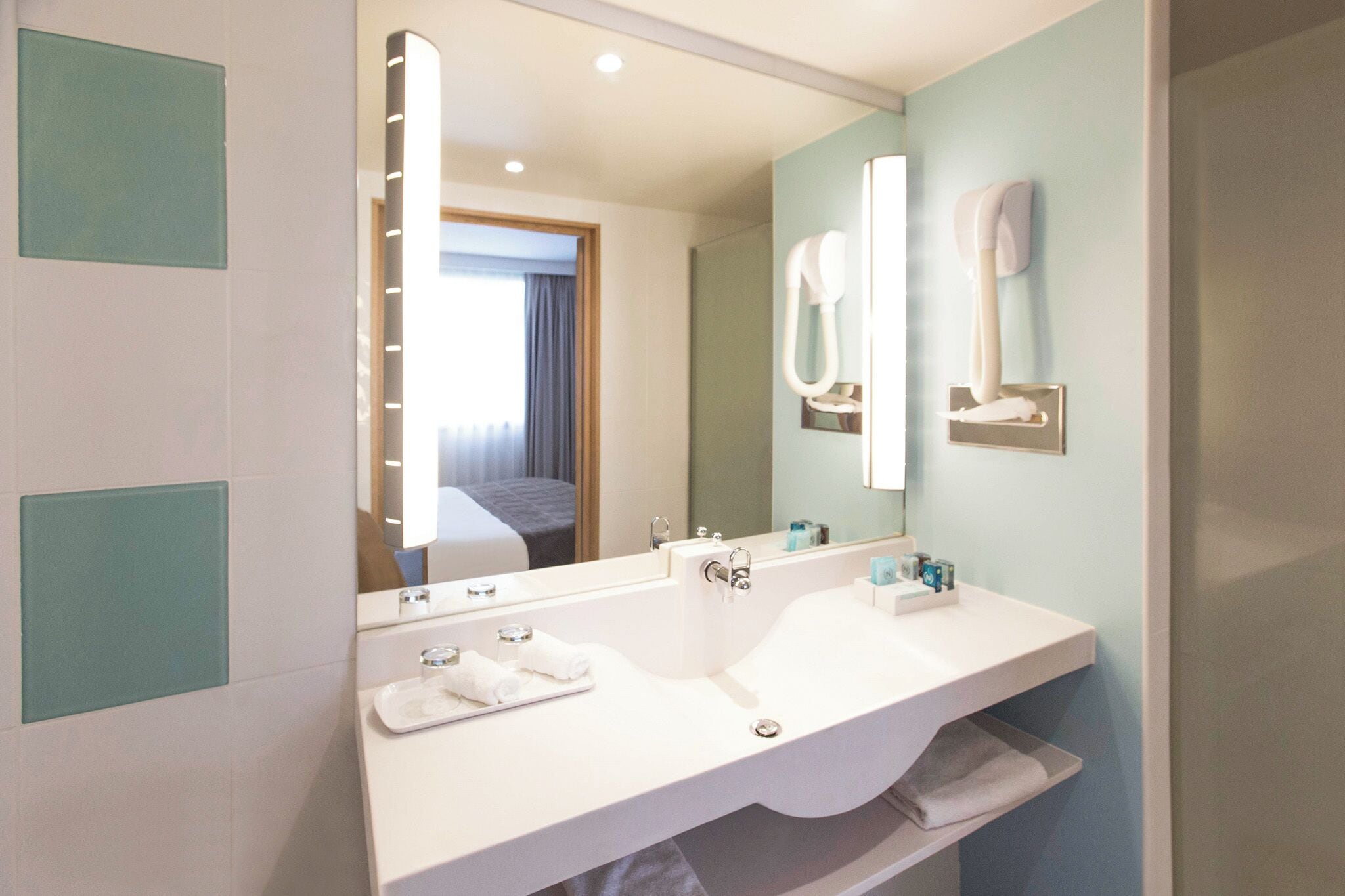A modern bathroom with a large mirror, two sinks, and a hairdryer mounted on the wall.