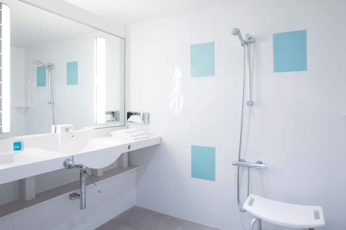 Un baño moderno con lavamanos, espejo y ducha blancos.