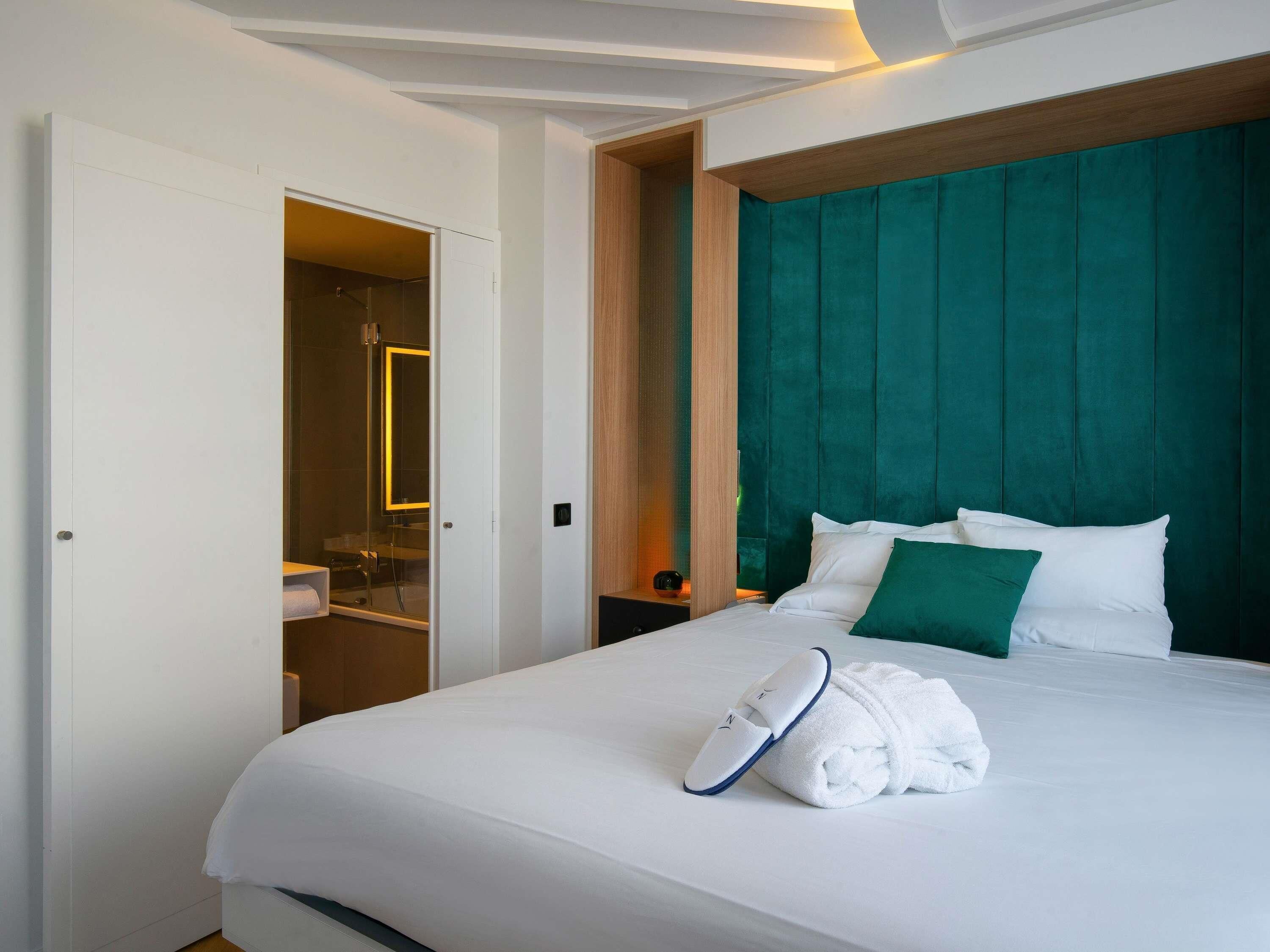 A hotel room with a bed, a bathroom, and a green upholstered headboard.