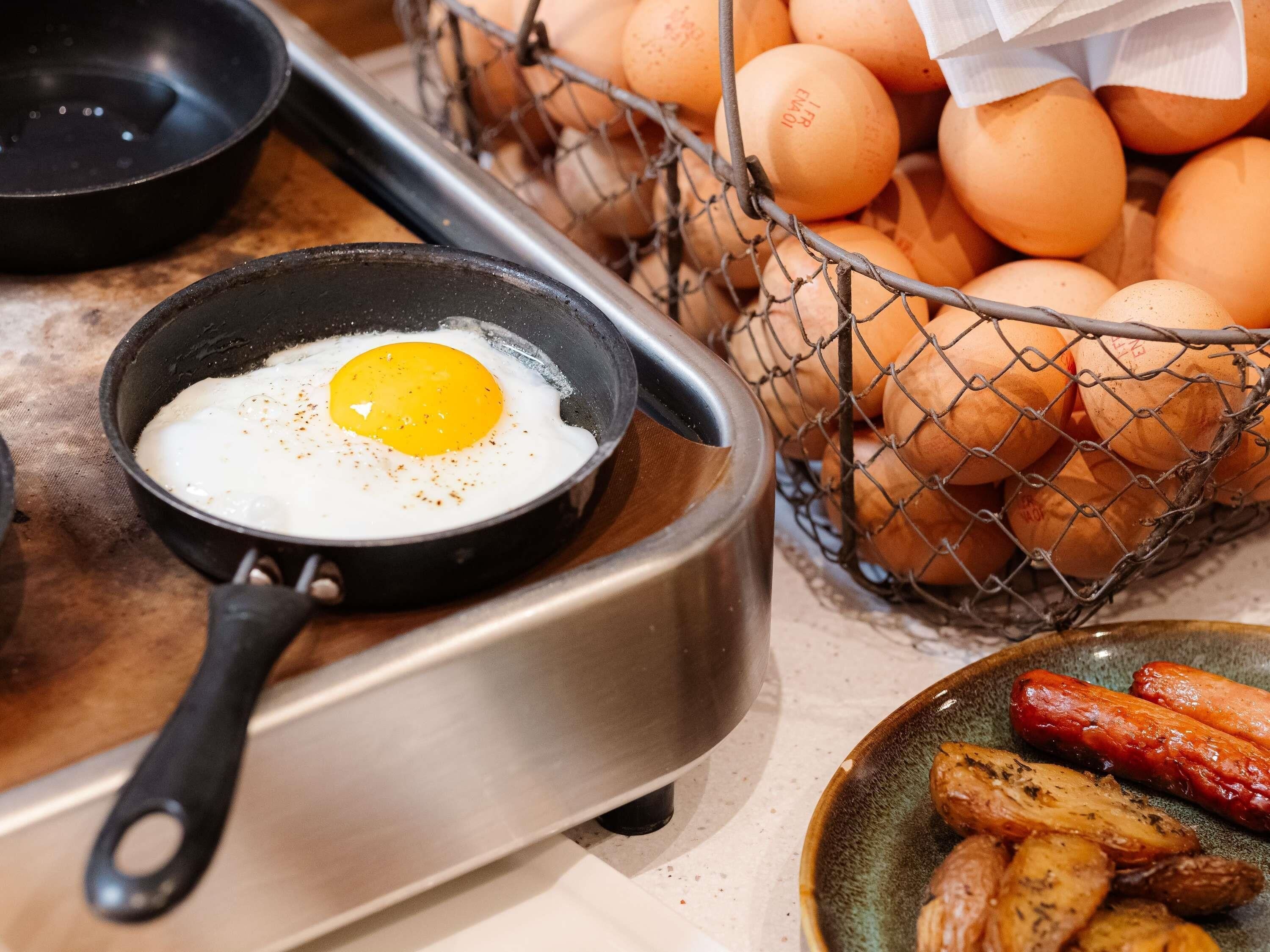 Una cocina con una sartén que contiene un huevo estrellado, una cesta de huevos y un plato de verduras asadas.