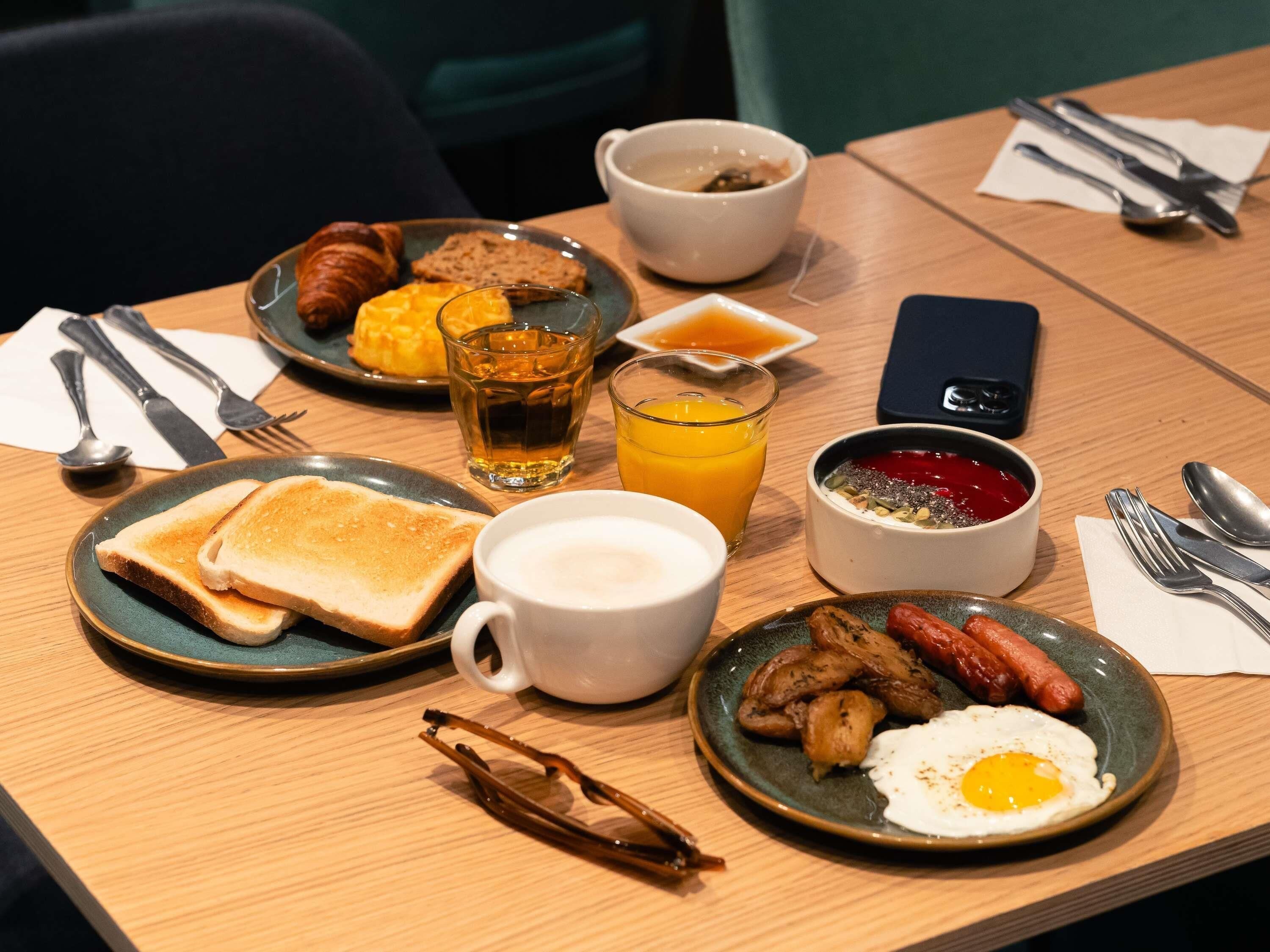 Une table de petit-déjeuner avec des tartines, des œufs, des saucisses et une tasse de café.