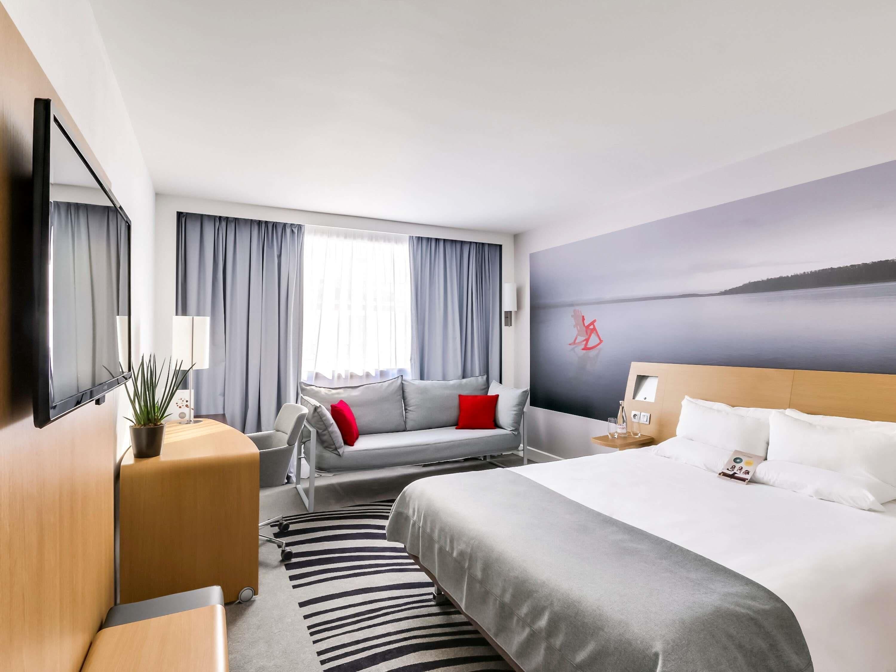 A modern hotel room with a large bed, a sofa, a desk, and a TV.