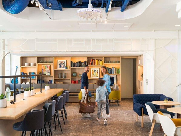 A modern interior with a long communal table, seating areas, and a bookshelf filled with books.
