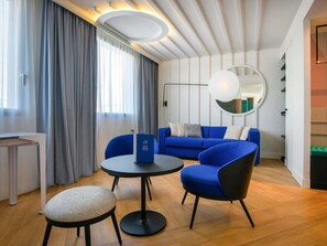 A modern hotel room with a blue sofa, a round table, and a small round chair.