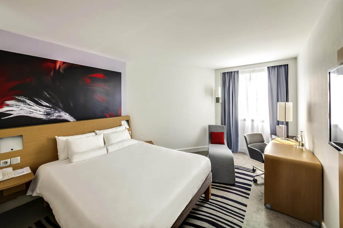 Una habitación de hotel con una cama grande, un escritorio, una silla, un televisor y un cuadro en la pared.