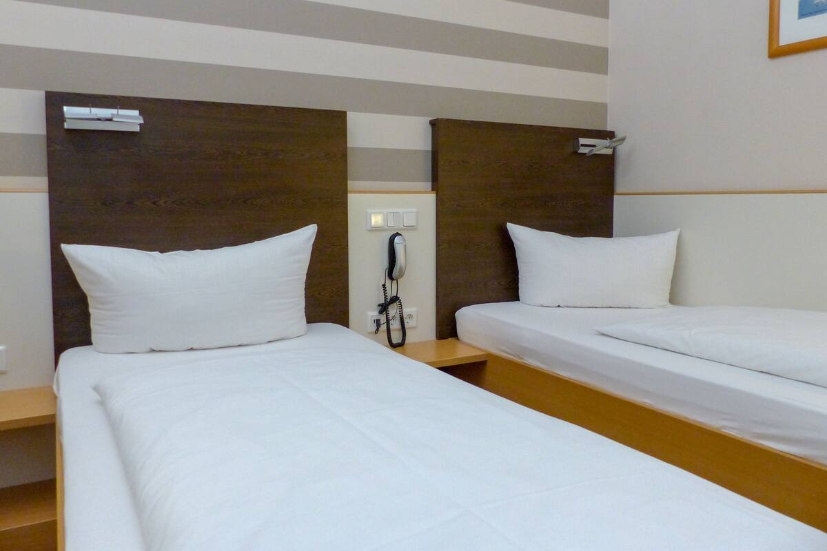 A hotel room with two single beds, wooden headboards, a bedside telephone, and a striped ceiling.
