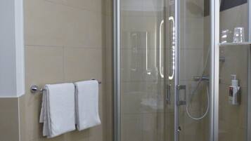 A glass-enclosed shower stall with a handheld showerhead and a handheld faucet.