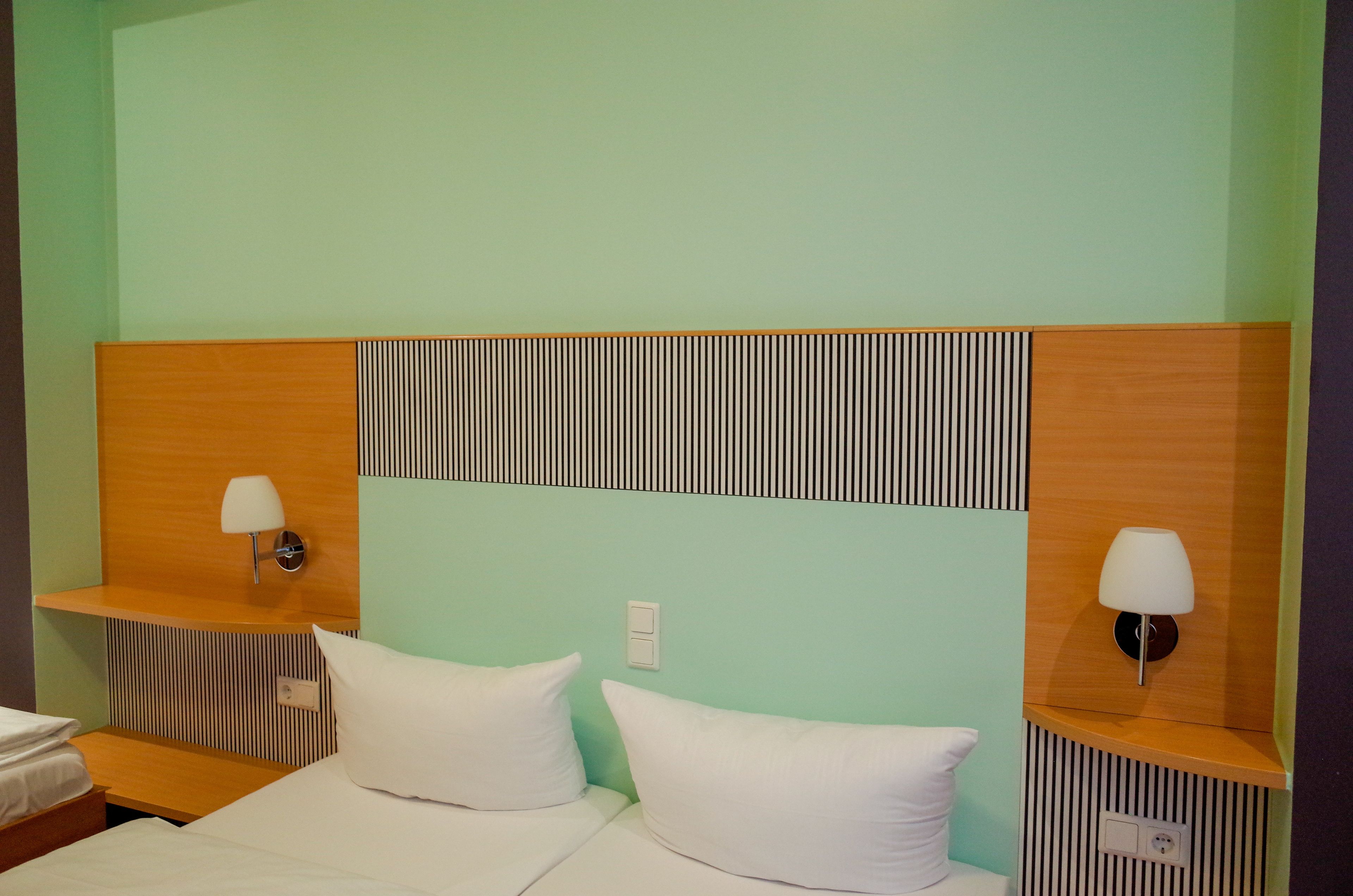 Hotellihuone, jossa on sänky, kaksi yöpöytää ja seinään kiinnitetty valaisin.