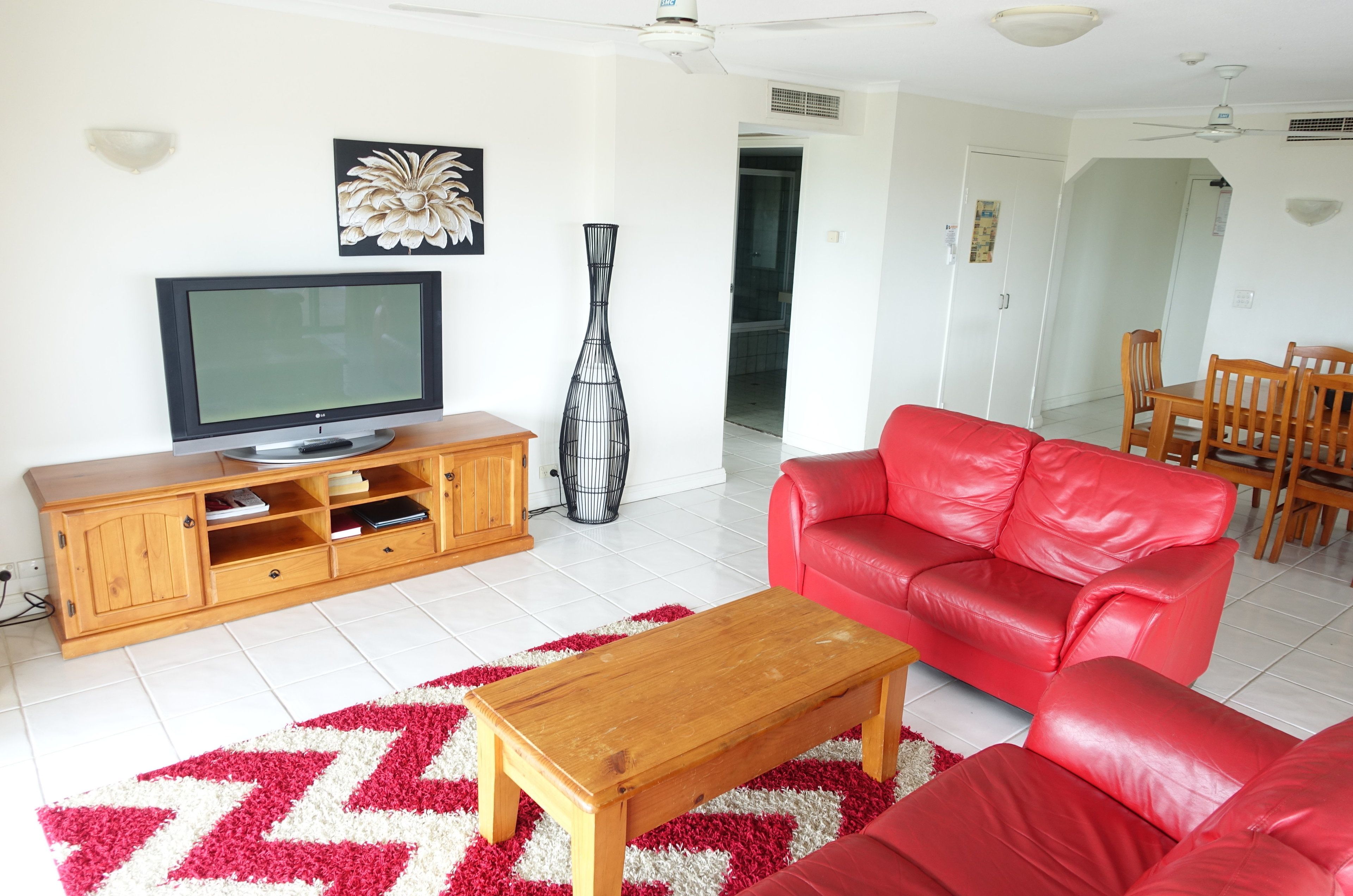A living room with a red leather sofa, a wooden coffee table, a flat-screen TV on a wooden cabinet, and a decorative vase.