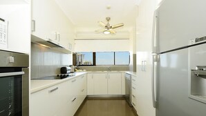A modern kitchen with white cabinets, a stainless steel refrigerator, a built-in oven, and a ceiling fan. - Marrakai Apartments (Darwin)