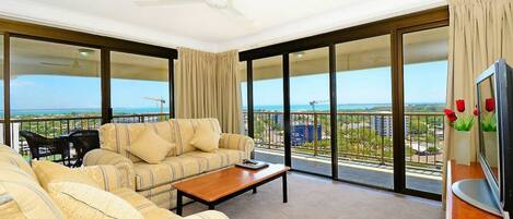 A spacious balcony with a sofa and a coffee table, large windows offering a view of the cityscape and construction cranes.