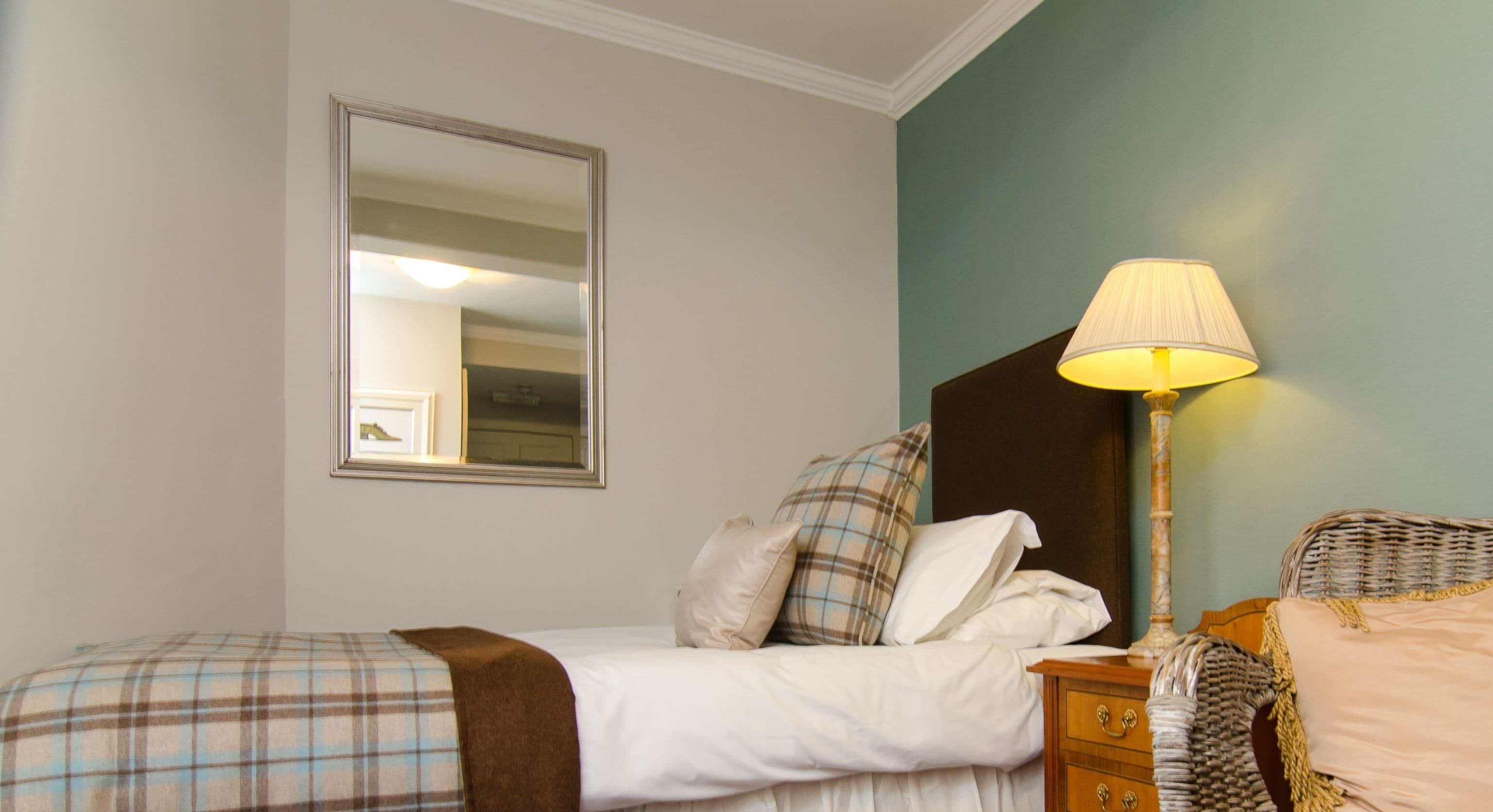 A bedroom with a bed, a nightstand, a lamp, a mirror, and a wall-mounted picture.