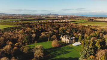A large estate with a prominent castle-like building surrounded by lush green fields and dense forests.