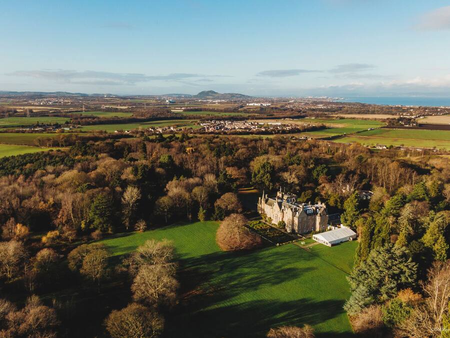 A large estate with a prominent castle-like building surrounded by lush green fields and dense forests.