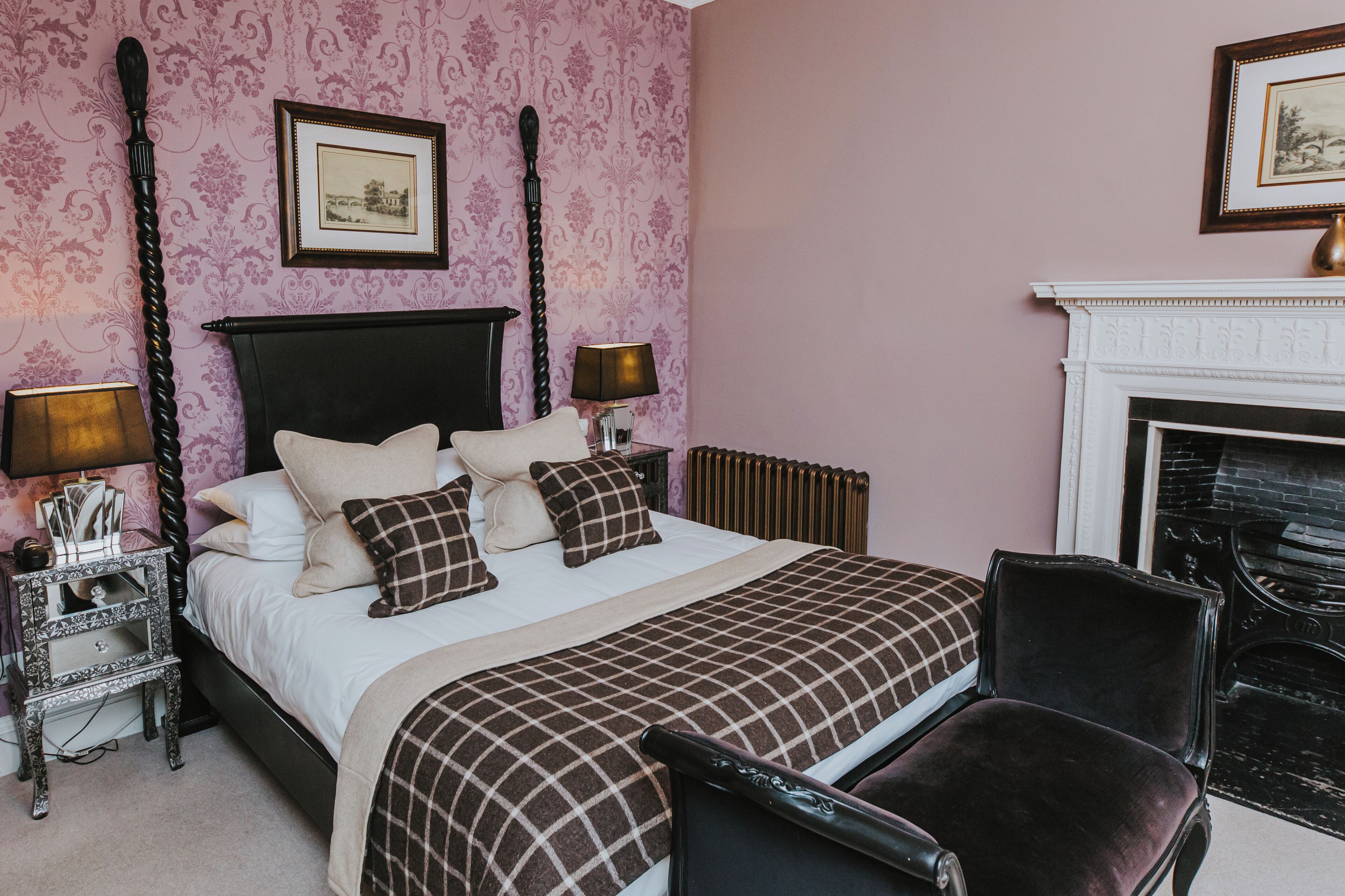 A bedroom with a four-poster bed, a fireplace, and a chair.