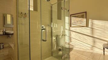 A modern bathroom with a glass-enclosed shower, a sink with a mirror, and a framed picture on the wall.