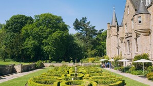 Un bâtiment historique doté d’un jardin à la française, comprenant un labyrinthe et une fontaine, ainsi qu’un chemin pavé.