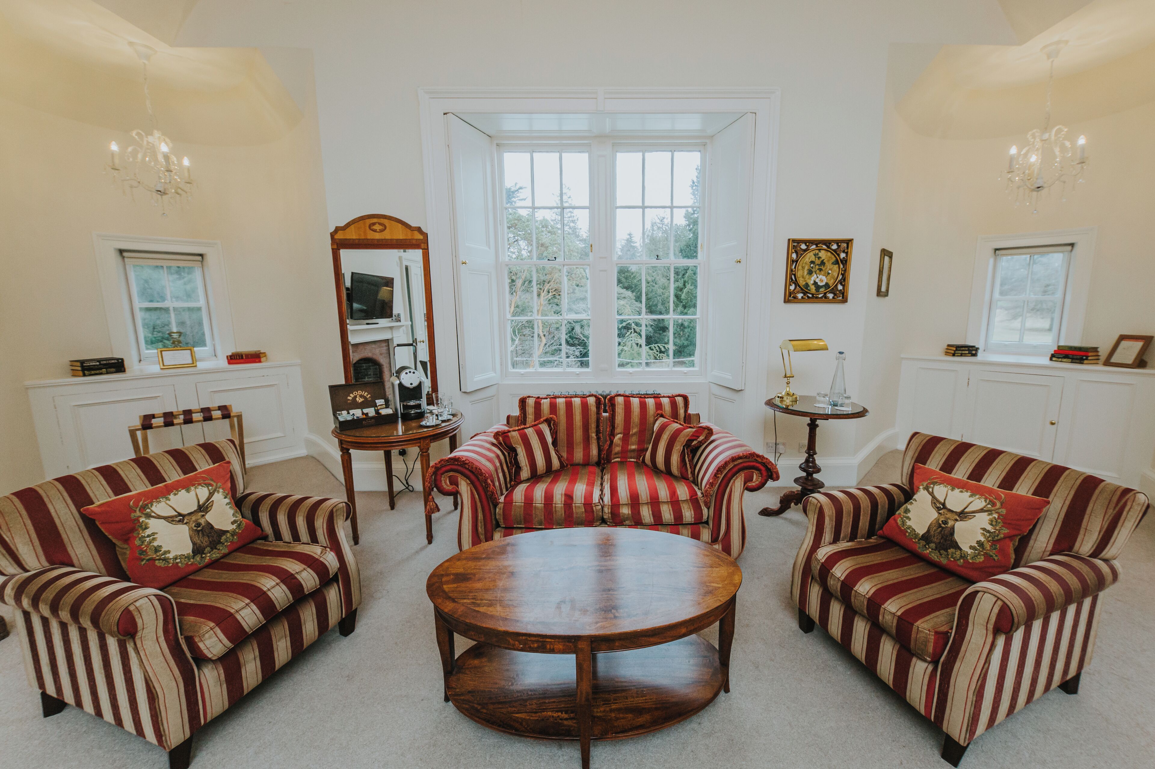 A room with two striped armchairs, a round coffee table, and a large window with a view of trees.