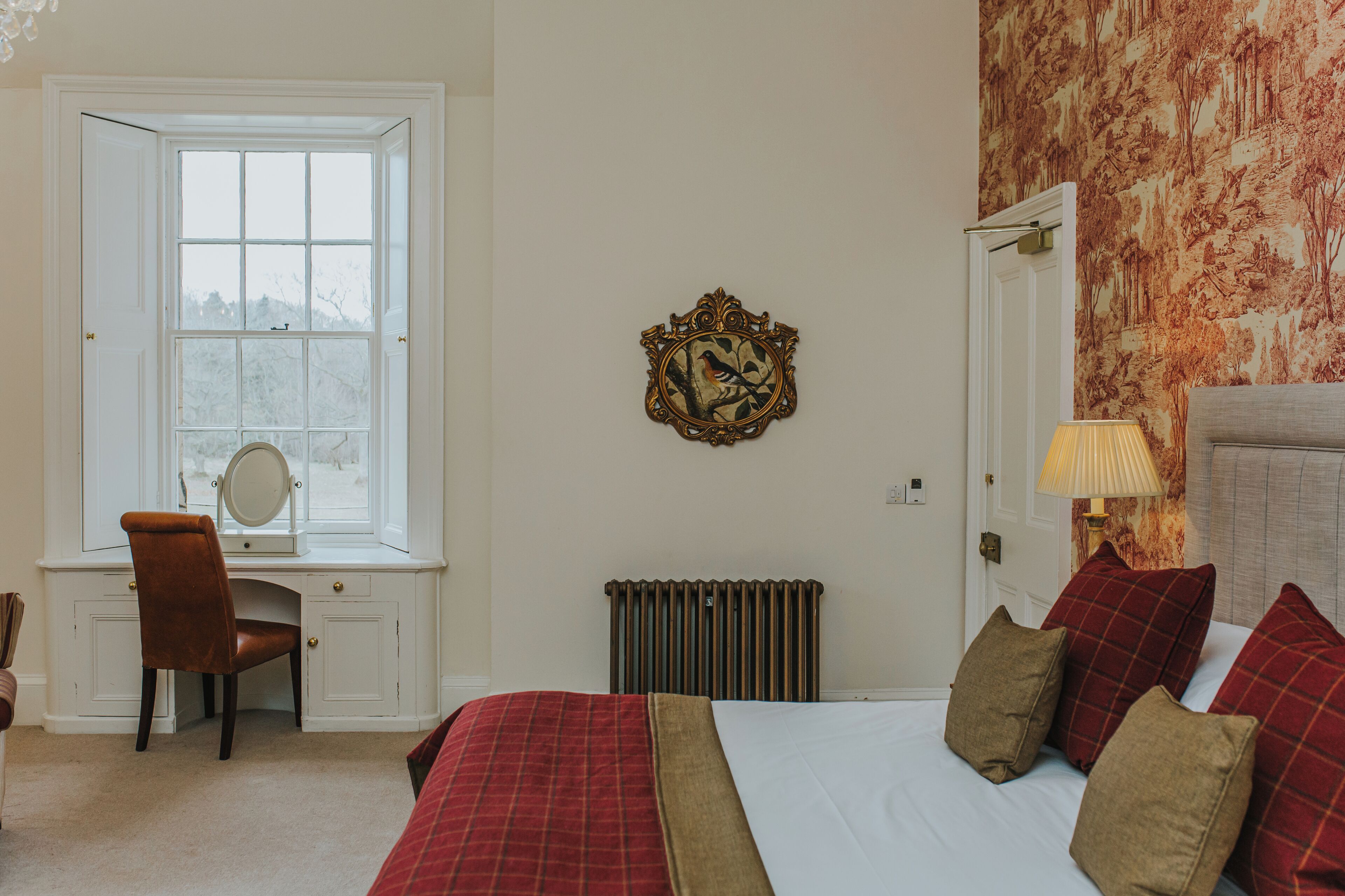 A bedroom with a bed, a desk with a chair, a radiator, and a window.