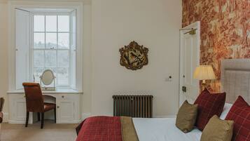 A bedroom with a bed, a desk with a chair, a radiator, and a window.