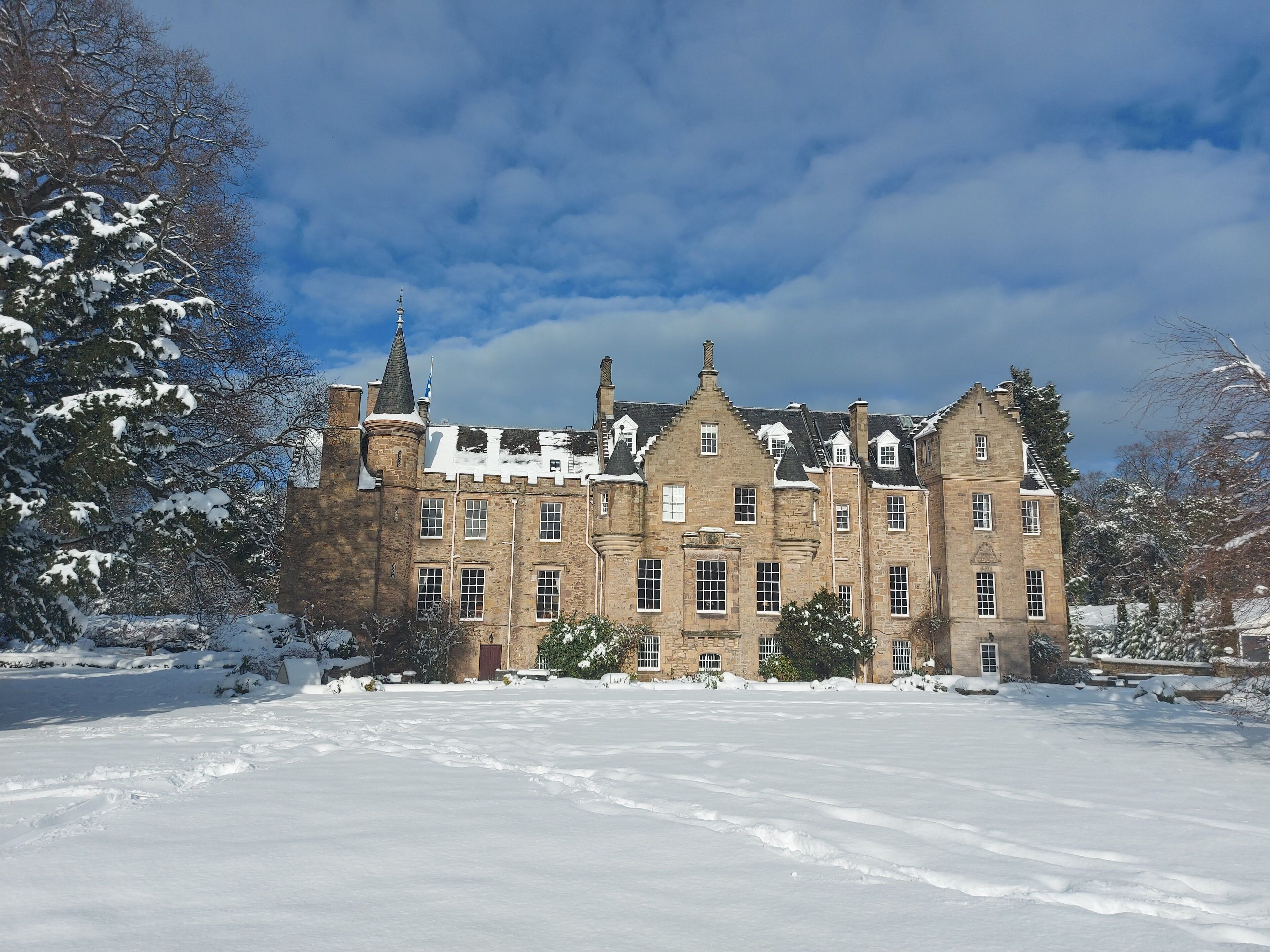 A large, historic stone building with multiple windows and a snow-covered landscape.