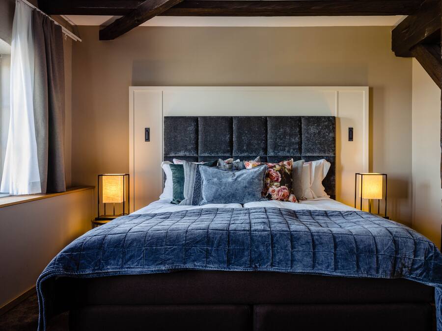 A large bed with a dark blue quilt, a headboard with a textured design, and two bedside lamps.
