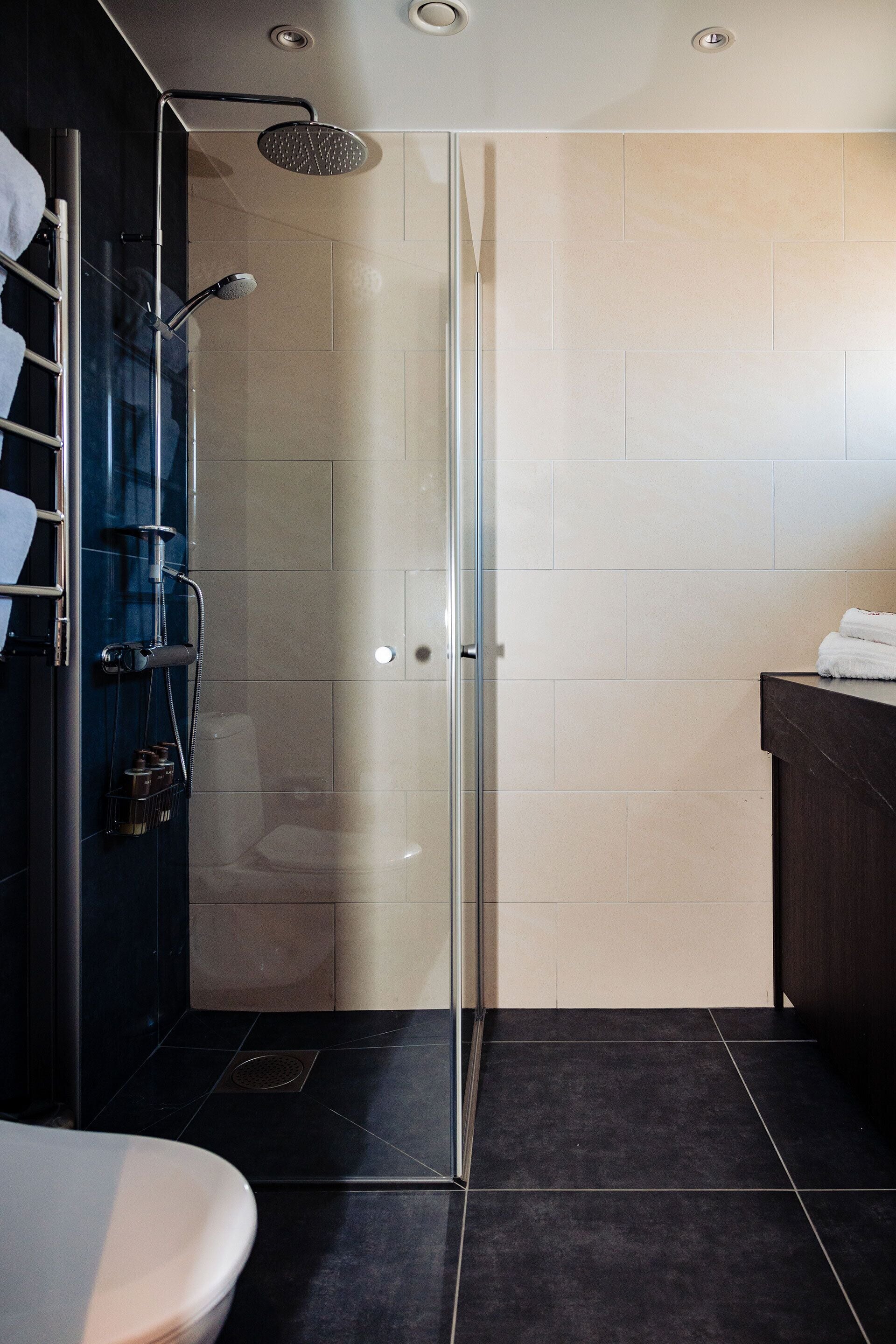 A modern bathroom with a glass-enclosed shower, a dark tiled floor, and a dark wooden vanity.