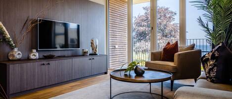 Una sala de estar moderna con un televisor de pantalla plana, muebles de madera oscura, una mesa redonda de centro y un sofá con cojines.