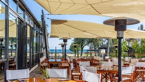 An outdoor dining area with tables and chairs, large umbrellas, and a view of the sea. - Hotel Skansen Båstad (Bastad)
