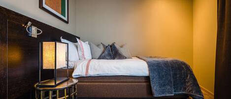 A neatly made bed with a dark blue blanket, a bedside lamp, and a small round table with a lamp.