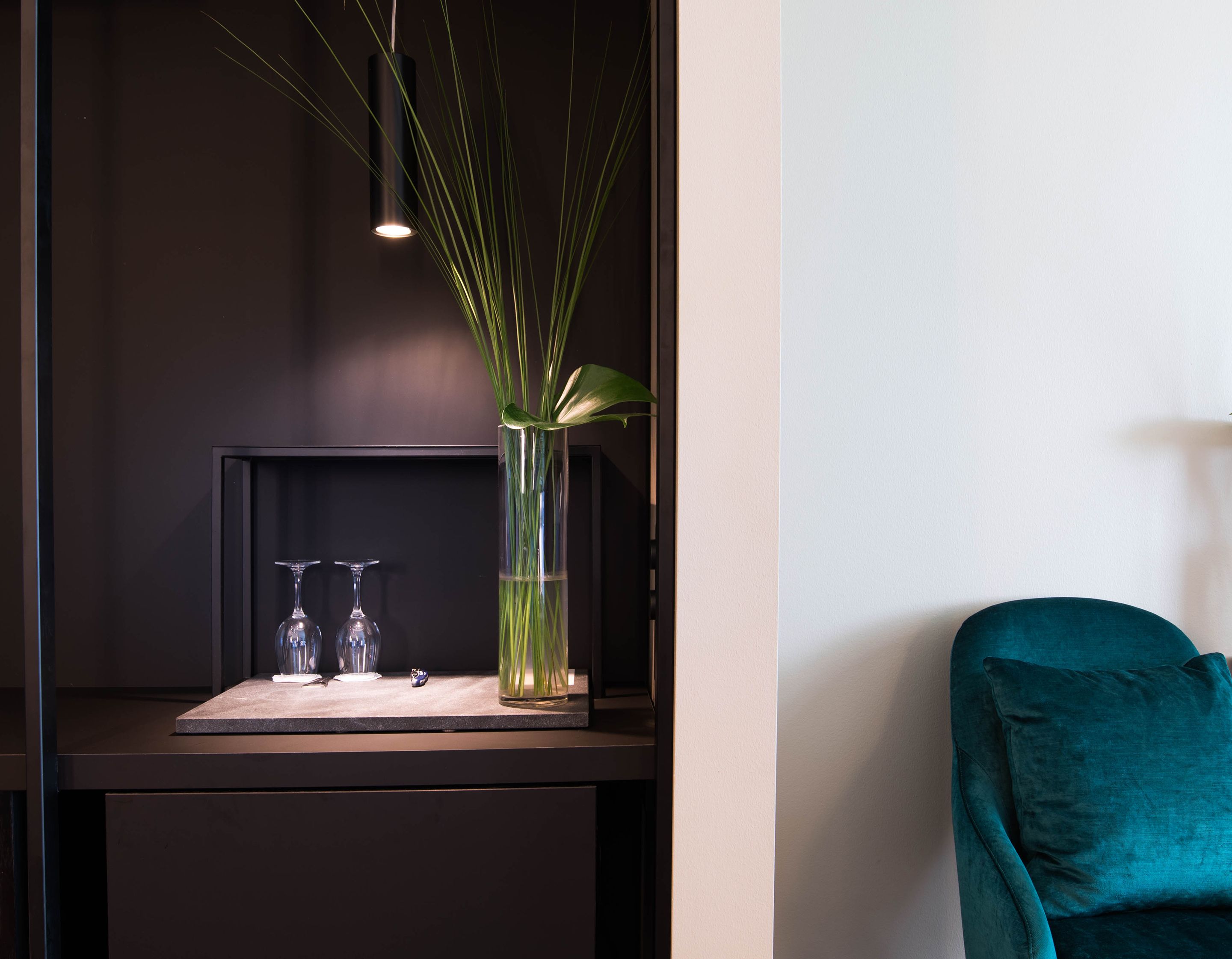 Une pièce moderne avec un bureau en bois foncé, une chaise turquoise et un vase contenant des plantes vertes.