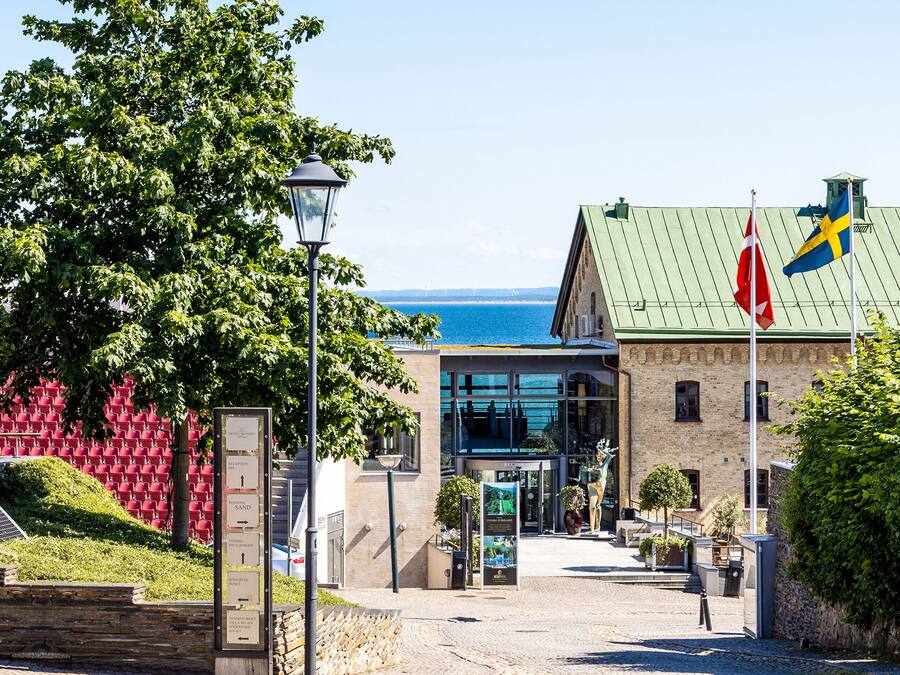 En byggnad med ett grönt tak, en flaggstång med flaggor och utsikt över havet.