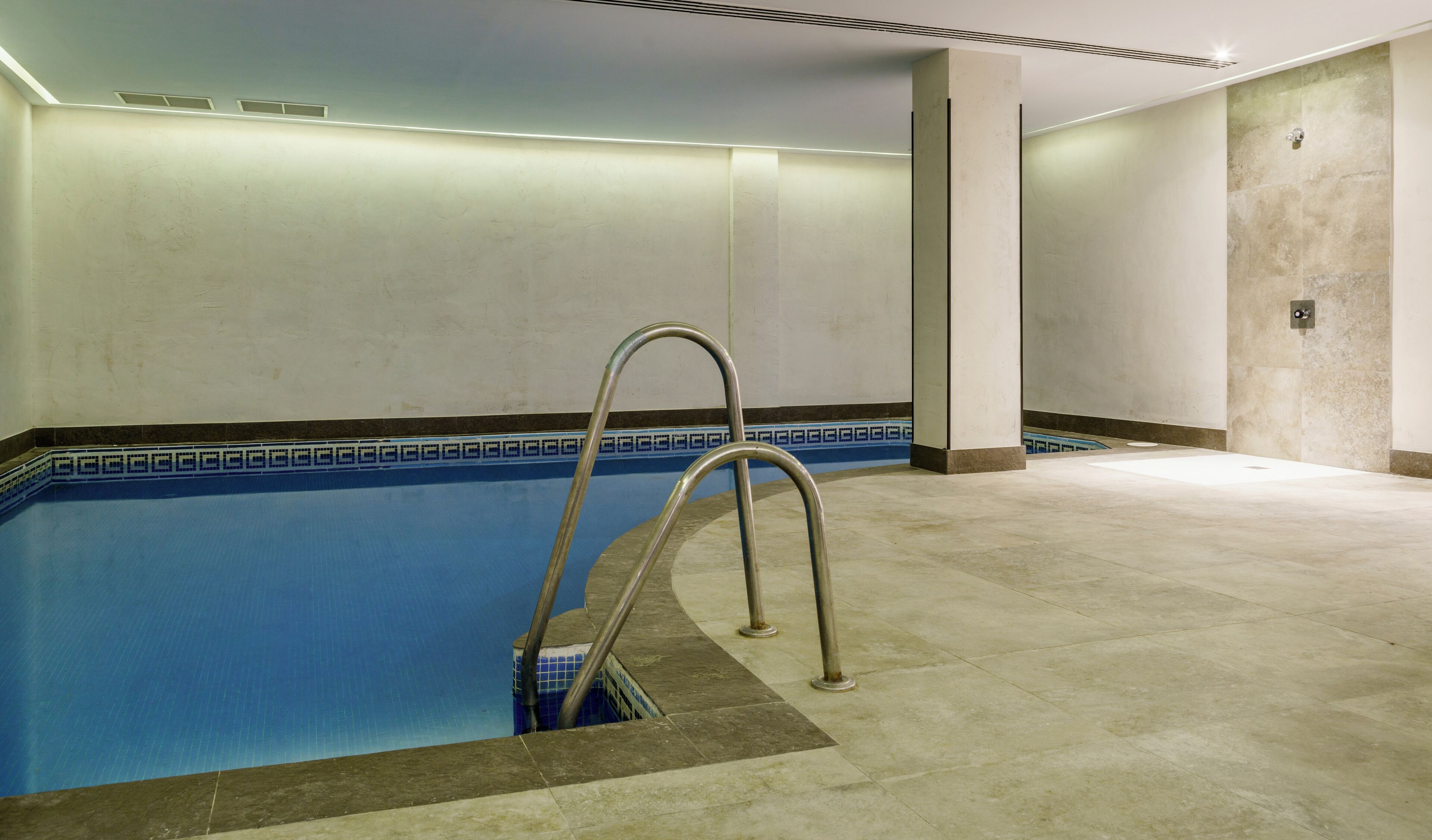 A swimming pool with a metal ladder, tiled walls, and a tiled floor.