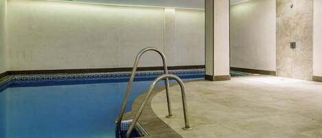 A swimming pool with a metal ladder, tiled walls, and a tiled floor.
