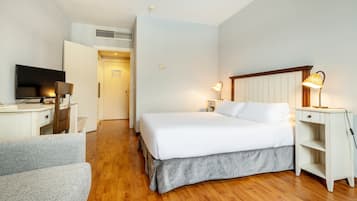 Una habitación de hotel con una cama, mesitas de noche, un escritorio con televisor, una silla y una lámpara.