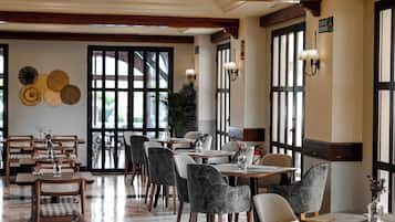 En restaurang med en modern inredning, med en blandning av trä- och stoppade stolar, bord dekorerade med mittpunkter och stora fönster som släpper in naturligt ljus.