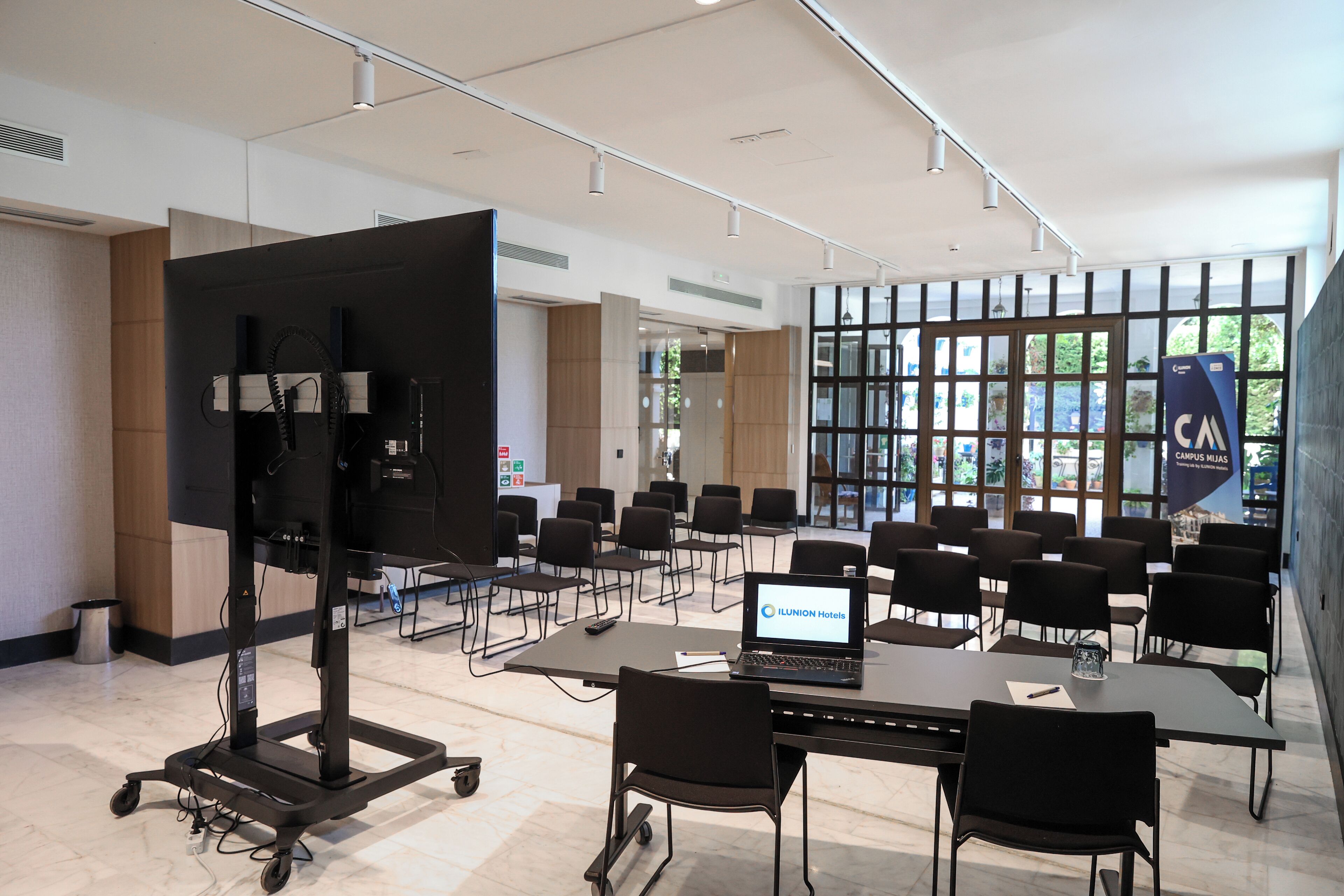 Una sala de conferencias con una pantalla grande, varias sillas, una computadora portátil y una mesa.
