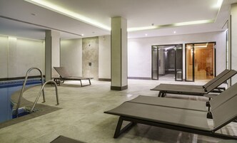 Moderni sisäuima-alue, jossa on aurinkotuoleja, uima-allas ja lasiseinöin erotettu spa-tila.