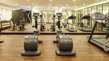 A gym with various exercise machines, including treadmills and stationary bikes, arranged in a spacious room with wooden flooring and large windows.