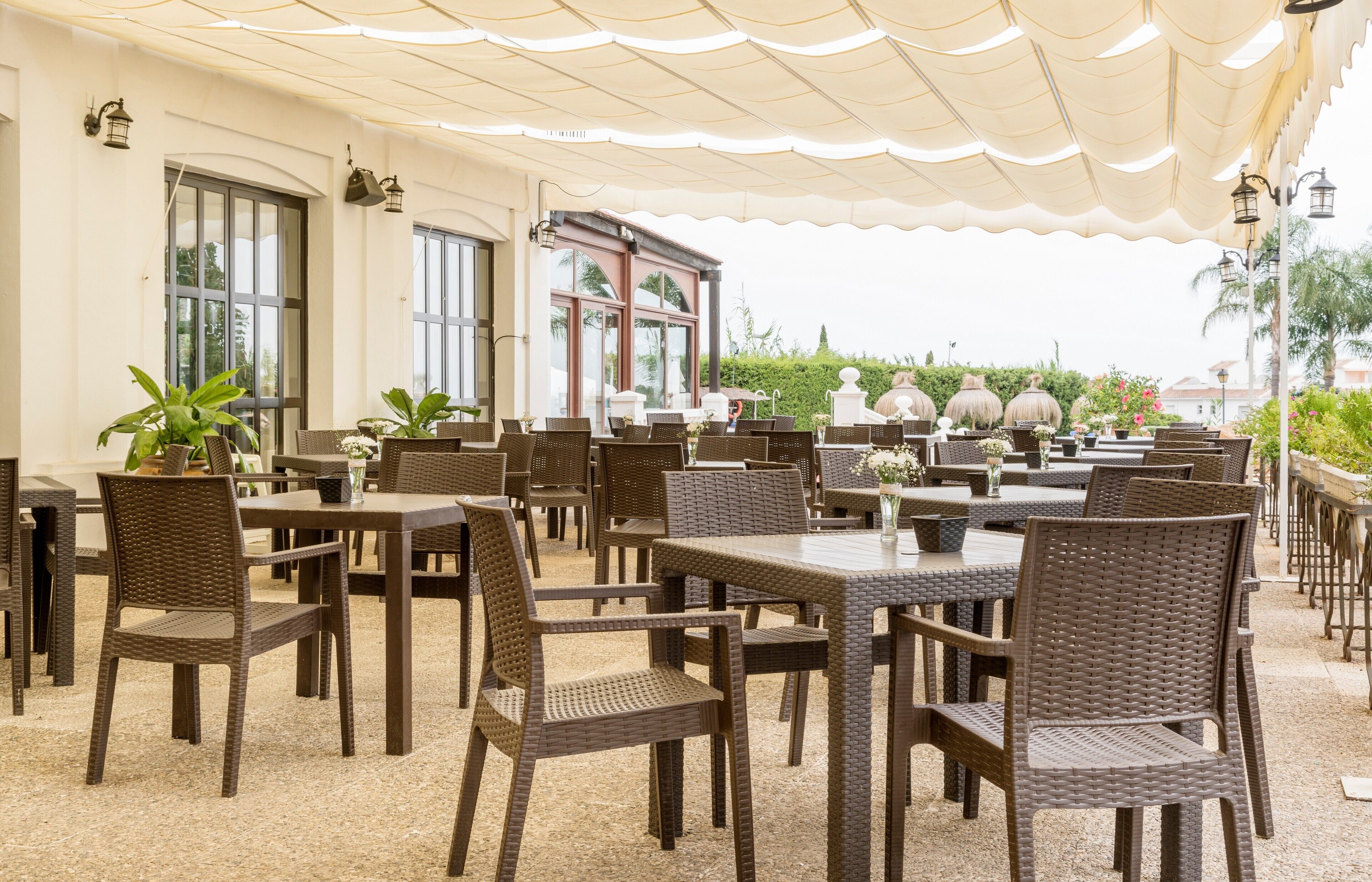 An outdoor patio with wicker furniture and tables, surrounded by large windows and a covered area.