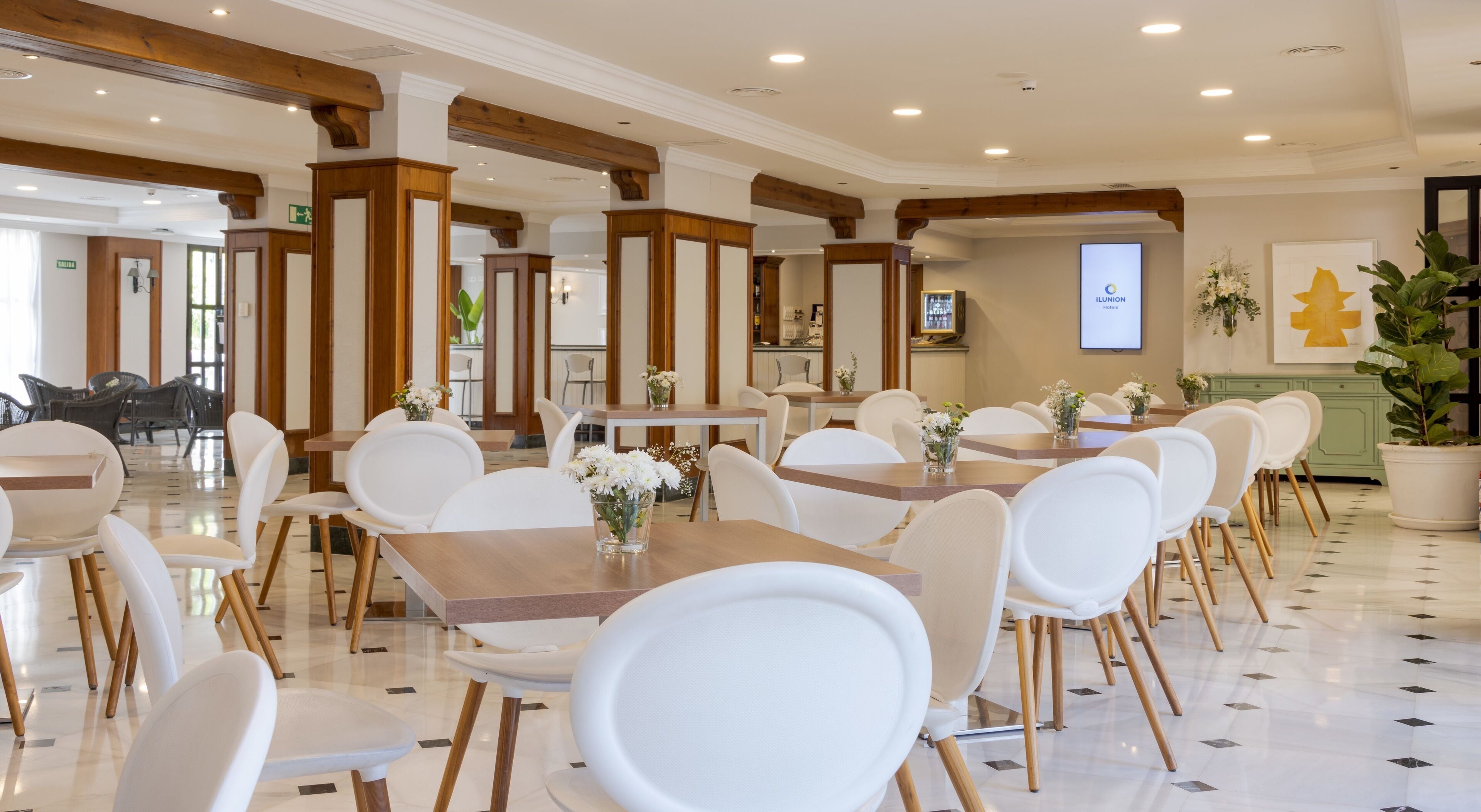 Une salle à manger d'hôtel avec des chaises et des tables blanches, des poutres en bois au plafond et une enseigne indiquant « Ilunion Hotels ».